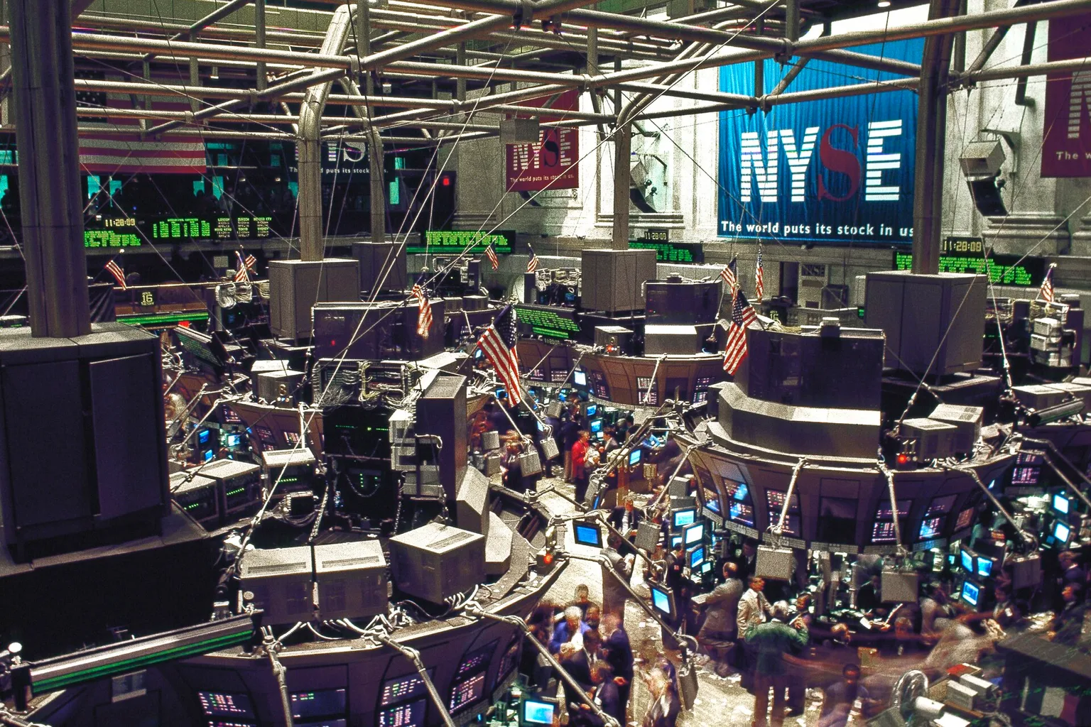 Traders on the New York Stock Exchange trading floor, under an NYSE banner and rows of green electronic price boards